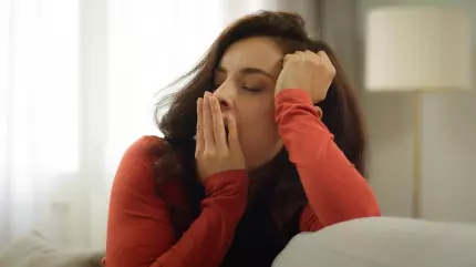Femeie cu părul şaten, îmbrăcată în roşu, care cască, obosită, pe o canapea Femeie cu părul şaten, îmbrăcată în roşu, care cască, obosită, pe o canapea